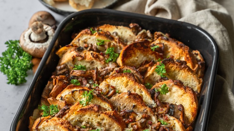 Überbackener Pilzauflauf mit knusprigen Brotscheiben, frischer Petersilie und Champignons in einer Auflaufform auf Holzbrett.