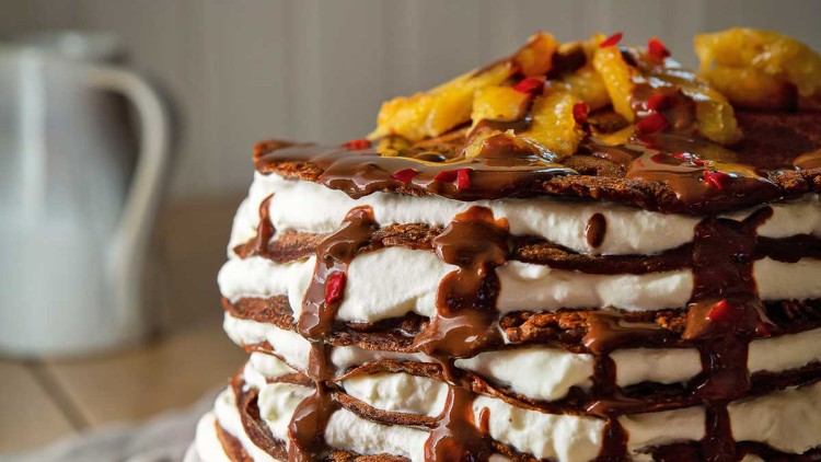 Schichttorte mit Sahne, Schokoladensoße, karamellisierten Obststücken und roten Streuseln auf einer weißen Tortenplatte.