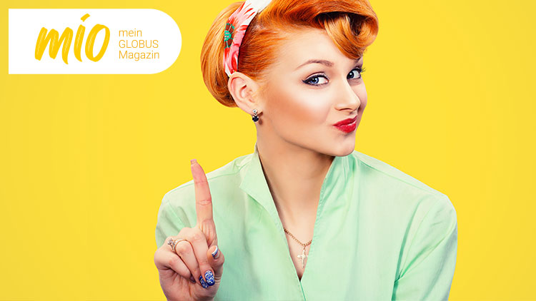 Person in mintgrünem Oberteil hebt den Zeigefinger, links oben steht „mio mein GLOBUS Magazin“ auf gelbem Hintergrund.