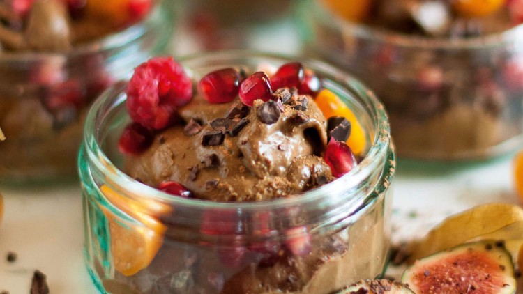 Schokoladen-Dessert in grünem Glas mit Himbeeren, Granatapfelkernen, Mandarinenstücken und halbierten Feigen dekoriert.