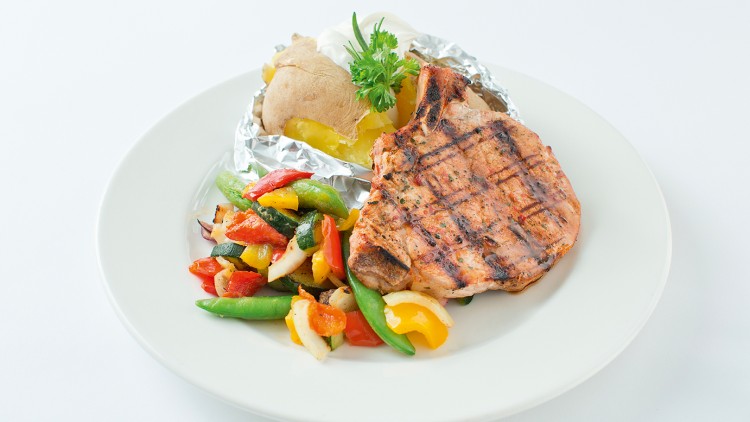 Gegrilltes Stück Fleisch, bunte Gemüsebeilage und Folienkartoffel mit Petersiliendeko auf weißem Teller.