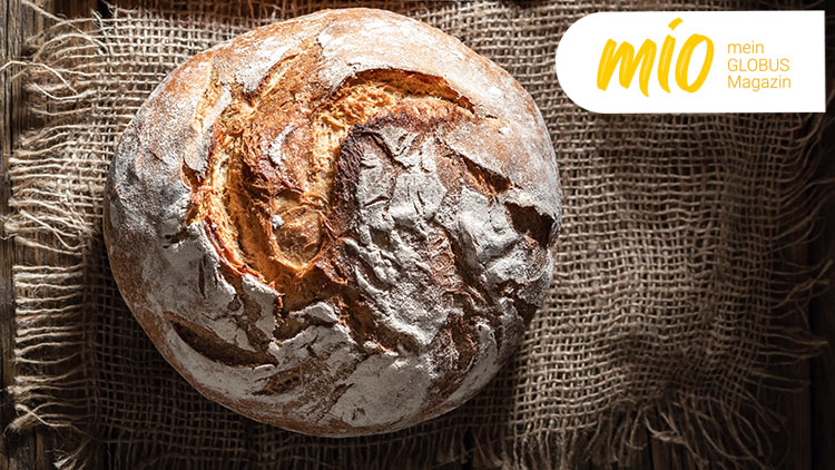 Rundes Bauernbrot mit knuspriger Kruste liegt auf Jutegewebe, oben rechts gelber Schriftzug „mio mein GLOBUS Magazin“.
