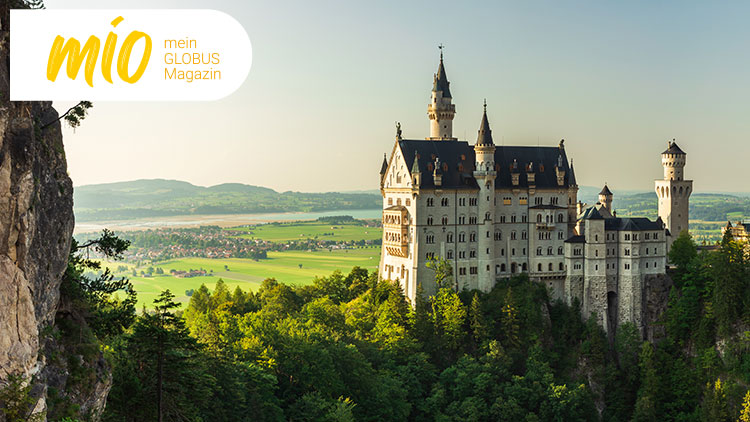Schloss Neuschwanstein vor grünem Tal und Hügeln, oben links Text „mio mein GLOBUS Magazin“ in Gelb und Orange.