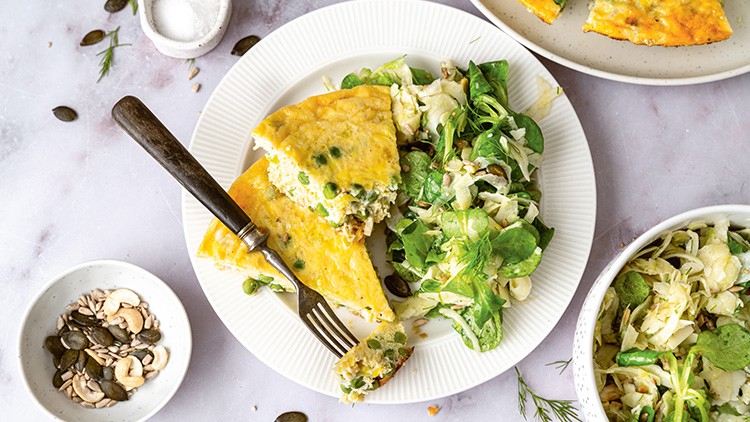 Omelett mit Erbsen auf einem weißen Teller, serviert mit frischem grünen Salat, daneben Schälchen mit Kernen und Salz.