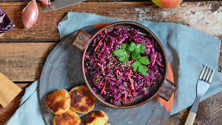 Rote-Bete-Salat mit Kräutern und Sesam in Schale, daneben goldbraune Bratlinge auf Teller, umgeben von Gemüse und Apfel.