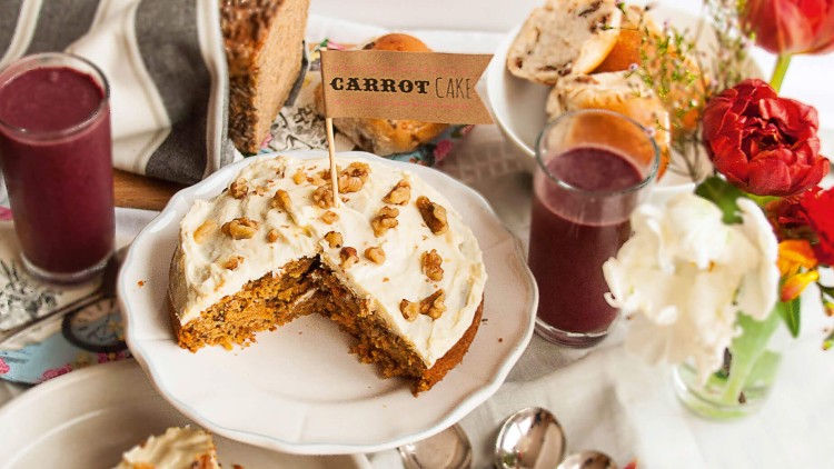 Karottenkuchen mit Walnüssen und Sahnehaube auf einer Tortenplatte, Schild mit der Aufschrift CARROT CAKE steckt darin.
