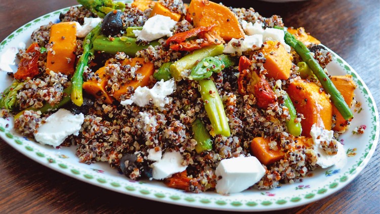 Ein Teller mit Quinoa, grünem Spargel, gebackenem Kürbis, getrockneten Tomaten, schwarzen Oliven und Feta-Stücken.