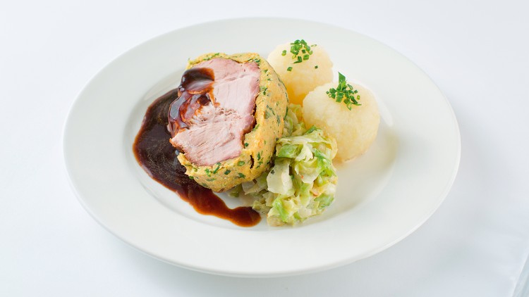 Auf einem weißen Teller liegen zwei Kartoffelklöße mit Schnittlauch, gefüllter Braten mit Sauce und eine Portion Rahmwirsing.