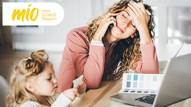 Person mit lockigem Haar hält einen Stift, auf einem Tisch liegt ein Laptop, rechts oben steht „mio mein GLOBUS Magazin“.