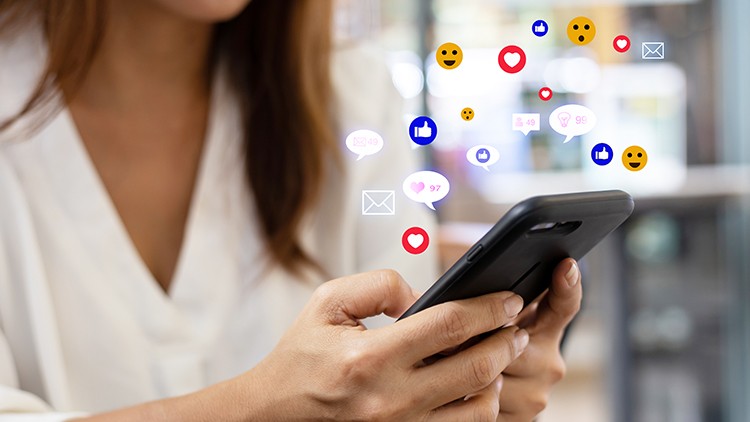 Person hält ein Smartphone in der Hand, darüber schweben digitale Symbole wie Herz, Smiley und Nachrichten.