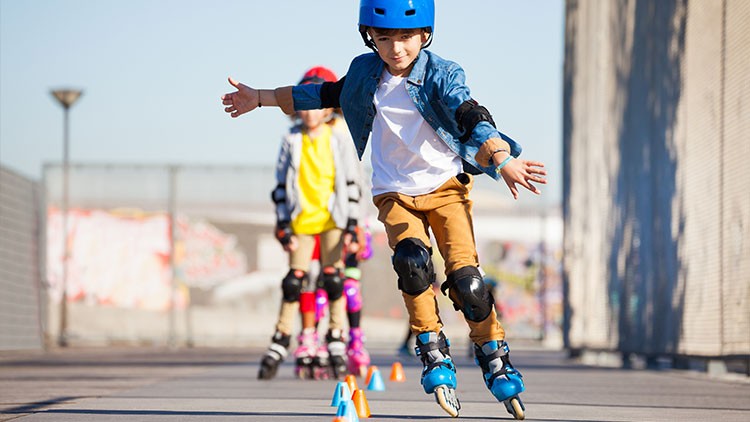 Person auf Inlineskates mit blauer Schutzkleidung fährt Slalom durch aufgestellte Hütchen, weitere Person im Hintergrund.