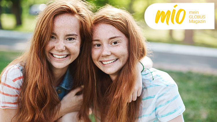 Zwei Personen mit langen roten Haaren sitzen eng beieinander im Grünen, rechts oben steht „mio mein GLOBUS Magazin“.