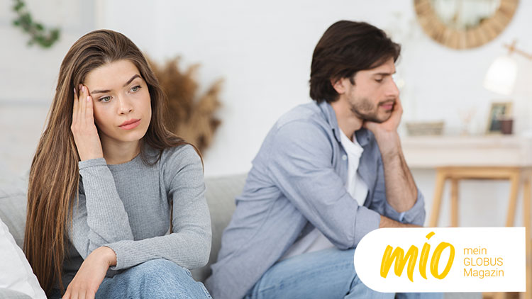 Zwei Personen sitzen in einem Wohnzimmer auf einem Sofa, unten rechts das mio mein GLOBUS Magazin-Logo in Gelb und Weiß.