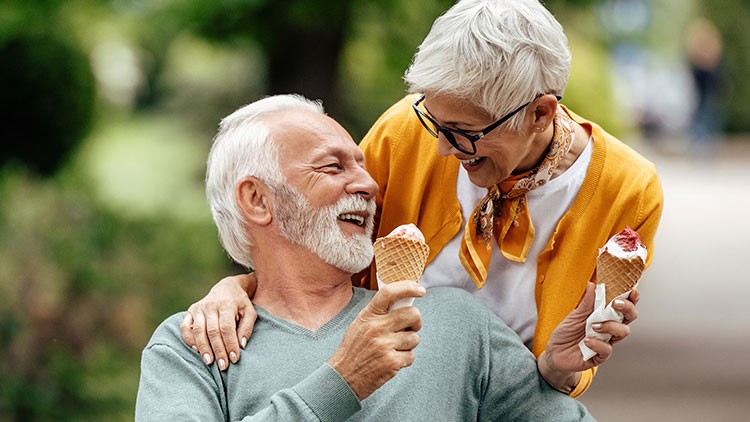 Zwei Personen halten jeweils eine Waffel mit bunt dekorierter Kugel Eis in einem grünen, parkähnlichen Umfeld.