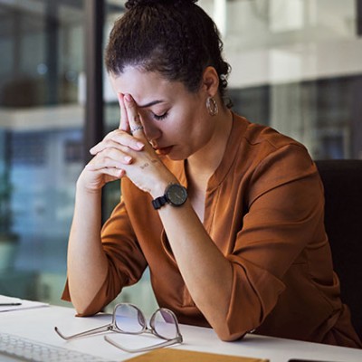Eine Frau mit Stress am Arbeitsplatz sitzt am Schreibtisch, den Kopf auf die Hände aufgestützt