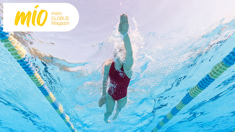 Person in rotem Badeanzug schwimmt in einem Schwimmbecken unter Wasser, links oben der Text mio mein GLOBUS Magazin.