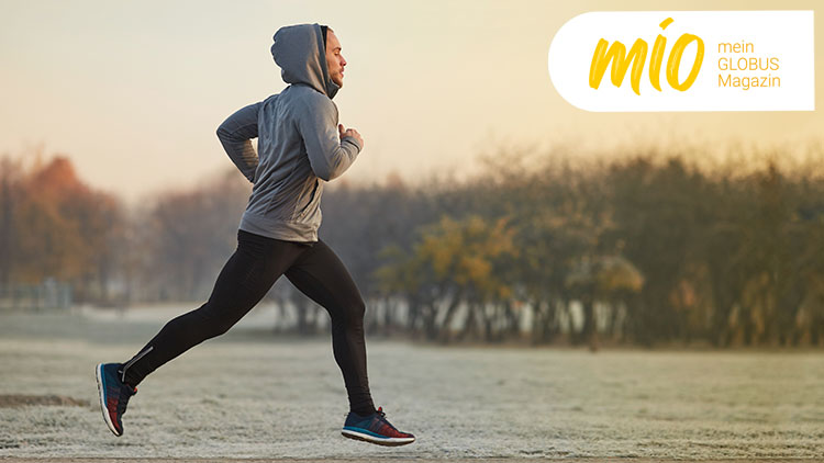 Person in grauem Hoodie und schwarzer Sporthose joggt vor herbstlicher Baumkulisse, Text „mio mein GLOBUS Magazin“ rechts oben.