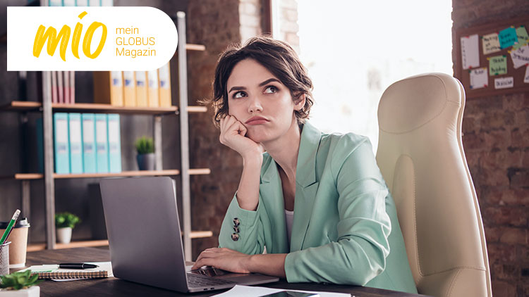 Person in hellgrünem Blazer sitzt an einem Schreibtisch, im Hintergrund Regale mit Aktenordnern und der Schriftzug mio mein GLOBUS Magazin.