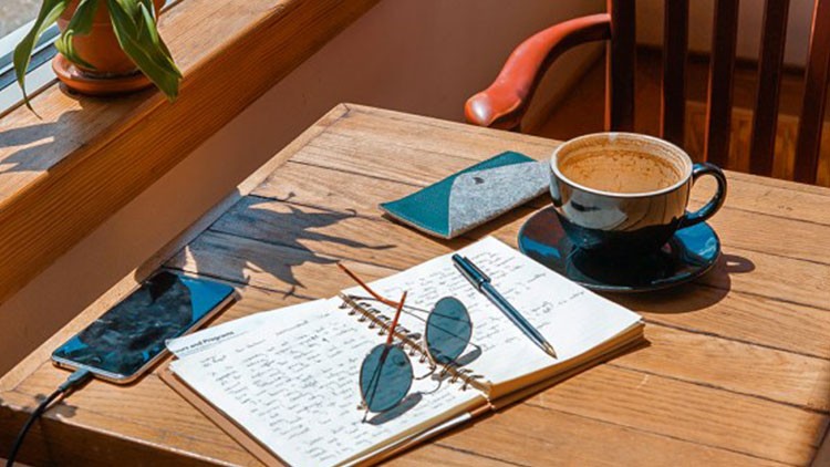 Tisch mit Notizbuch, Tasse, Sonnenbrille, Handy