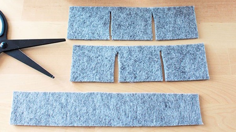Grauer Filzstoff auf Holztisch, oben und mittig in Rechtecke geschnitten, rechts schwarze Schere.