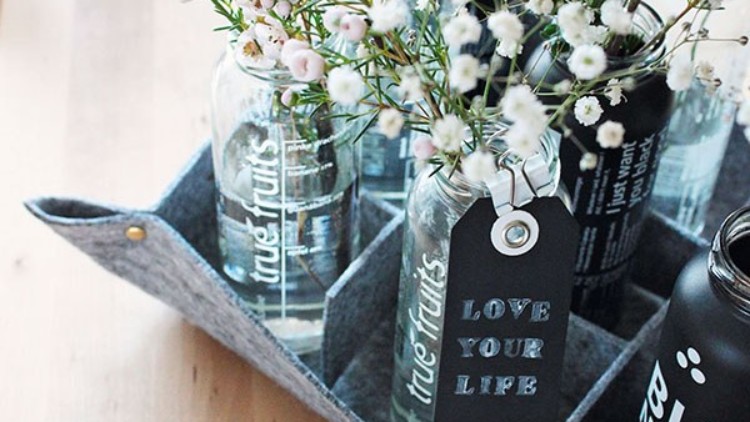 Mehrere Glasflaschen mit der Aufschrift „true fruits“ stehen in einer Filztasche, eine Flasche trägt ein Etikett mit „LOVE YOUR LIFE“.