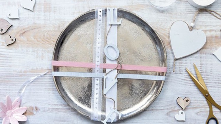 Silbernes Tablett ist mit weißen und rosa Bändern sowie den befestigten Buchstaben L-O-V-E dekoriert.