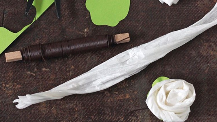 Weiße Papierrose, brauner Draht auf Holzspule und grüne Papierformen liegen auf einem dunklen Untergrund.