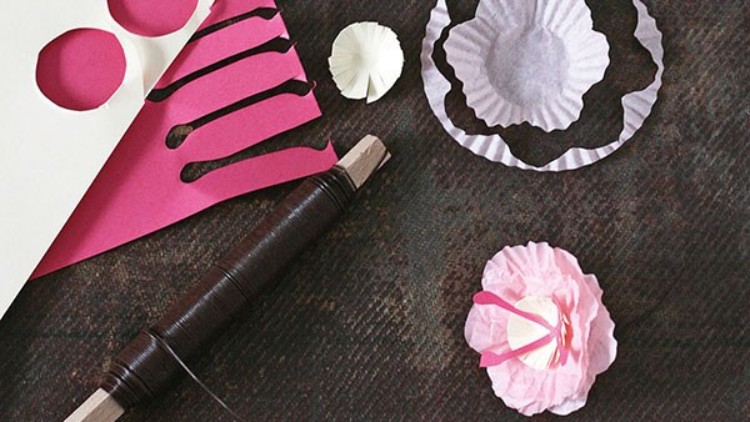 Verschiedene Bastelmaterialien wie Draht, farbiges Papier und Papierblumen liegen auf einer dunklen Oberfläche.