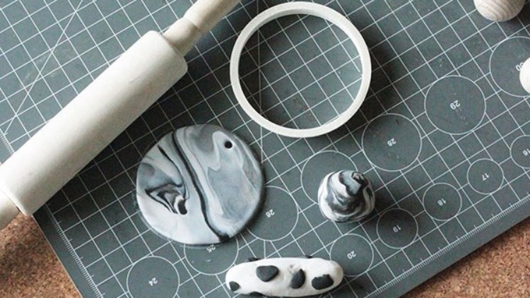Eine Marmorrolle, Tonformen in Grau und Weiß sowie ein runder Ausstecher liegen auf einer Schneidematte mit Rastermuster.