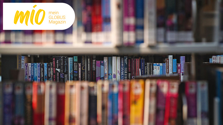 Regale mit zahlreichen Büchern in verschiedenen Farben und Formaten im Fokus, oben links das mio mein GLOBUS Magazin-Logo.