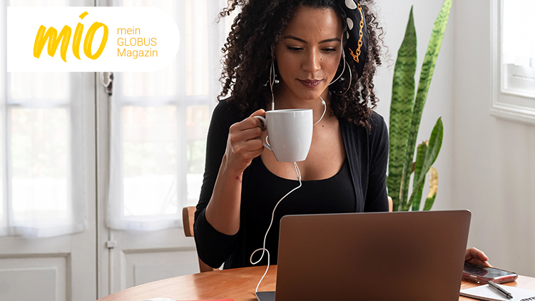 Person hält eine weiße Tasse, trägt Kopfhörer und arbeitet an einem Laptop, links oben steht „mio mein GLOBUS Magazin“.