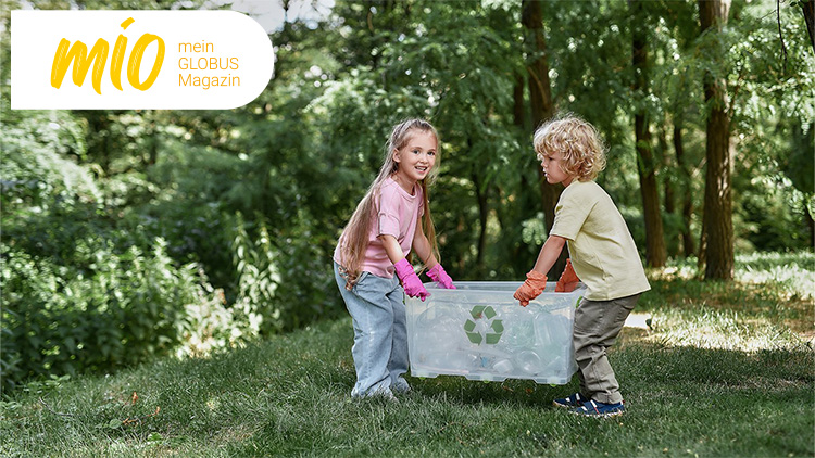 Zwei Kinder tragen im Wald eine durchsichtige Box mit Recycling-Symbol, darin befinden sich leere Plastikflaschen.
