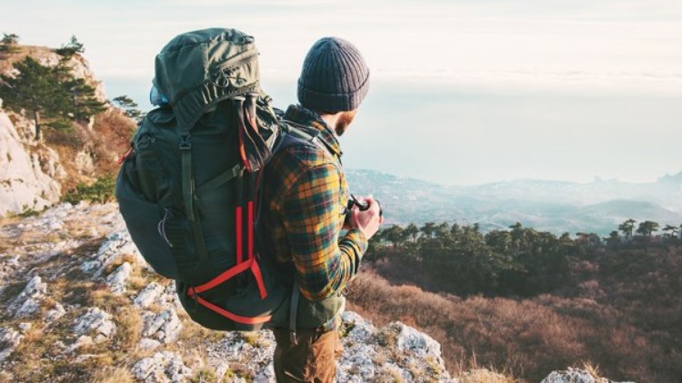 Mann mit Rucksack blickt von einem Berg ins Tal