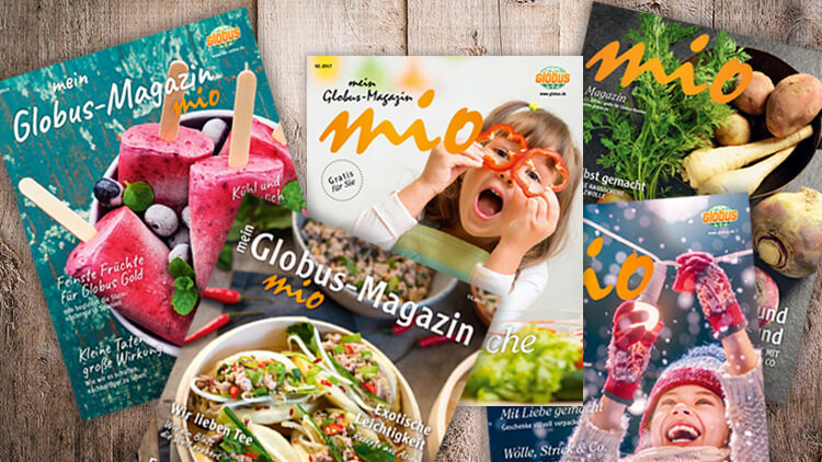 Mehrere Ausgaben des mein GLOBUS-Magazins „mio“ liegen überlappend auf einem Holzuntergrund.