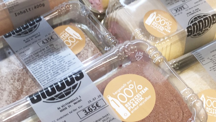 Mehrere rechteckige Kuchenschalen mit GLOBUS-Logo, Preisschildern und Hinweis „100% recyceltem Plastik“ auf gelbem Aufkleber.