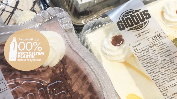 Kuchenauswahl in transparenten Verpackungen mit GLOBUS-Logo, Preisschildern und Hinweis „100% recyceltem Plastik, erneut recycelbar“.