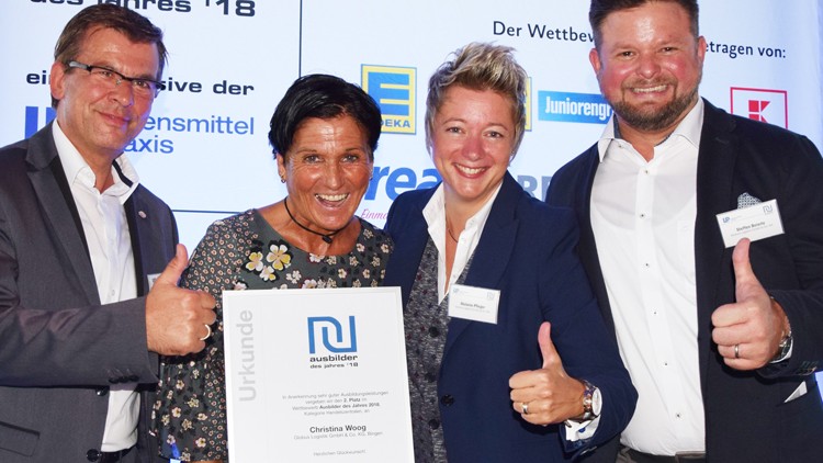 Vier Personen in Geschäftsbekleidung halten gemeinsam eine Urkunde mit der Aufschrift „Ausbilder des Jahres ’18“.