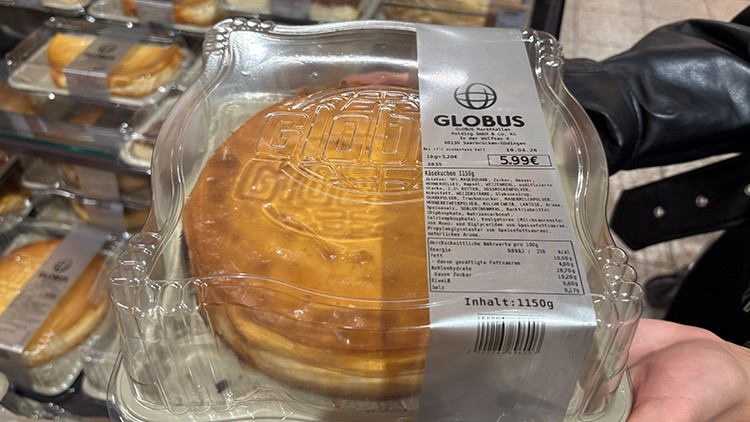 In einer durchsichtigen Plastikverpackung ist ein Käsekuchen mit GLOBUS Schriftzug, daneben ein Etikett mit Produktinformationen sichtbar.