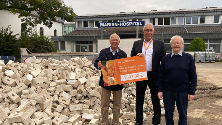 Drei Personen halten einen Spendenscheck der GLOBUS-Gruppe über 150.000 Euro vor einem Gebäude mit dem Schild Marien-Hospital.