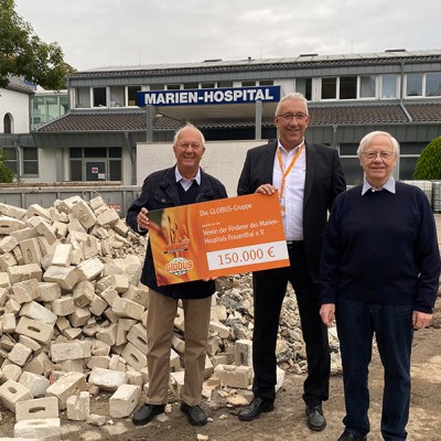 Drei Personen halten einen Spendenscheck der GLOBUS-Gruppe über 150.000 Euro vor einem Gebäude mit dem Schild Marien-Hospital.