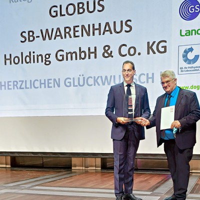 Zwei Männer in Anzügen stehen vor einer Leinwand mit der Aufschrift GLOBUS SB-WARENHAUS Holding GmbH & Co. KG.