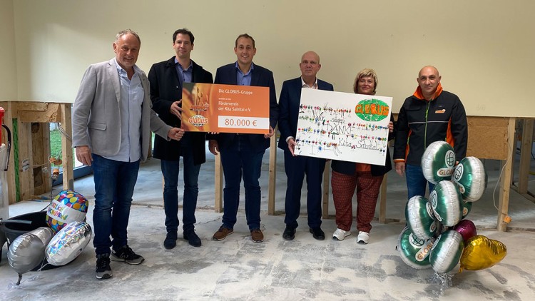 Sechs Personen halten zwei große Tafeln mit 80.000 Euro und einem Dankeschriftzug, daneben GLOBUS-Luftballons und Geschenke.