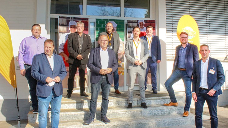 Mehrere Personen in Businesskleidung stehen auf Steinstufen vor einem Eingang mit zwei gelben GLOBUS-Werbebannern.