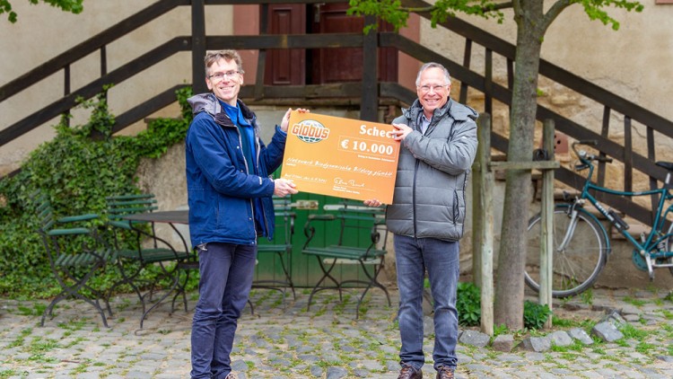 Zwei Personen halten einen großen Scheck mit GLOBUS-Logo und der Aufschrift „10.000 €“ vor einer Außenkulisse.