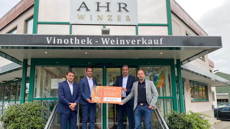 Vier Personen halten vor einem Gebäude mit der Aufschrift „Ahr Winzer Vinothek - Weinverkauf“ einen Scheck über 20.000 €.