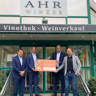 Vier Personen halten vor einem Gebäude mit der Aufschrift „Ahr Winzer Vinothek - Weinverkauf“ einen Scheck über 20.000 €.