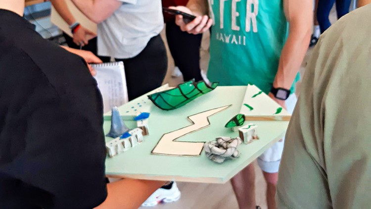 Mehrere Personen stehen zusammen, eine Person hält ein Modell mit grünen und weißen Elementen sowie verschiedenen Formen in der Hand.