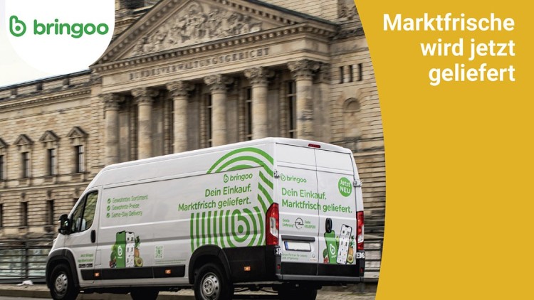 Ein weißer bringoo-Lieferwagen mit grünem Logo und Schriftzug „Dein Einkauf, Marktfrisch geliefert“ steht vor einem historischen Gebäude.