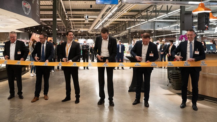 Sechs Personen schneiden ein gelbes Band mit GLOBUS-Logo vor Publikum in einem Marktbereich durch.