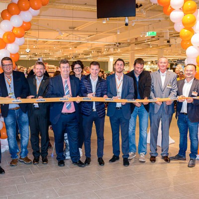 Mitarbeitende stehen unter einem orangenen und weißen Luftballonbogen und halten ein Band mit GLOBUS-Logo zur Eröffnung.